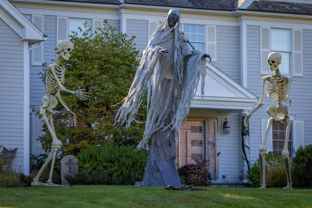 An oversized skeleton figure standing above a suburban house at dusk