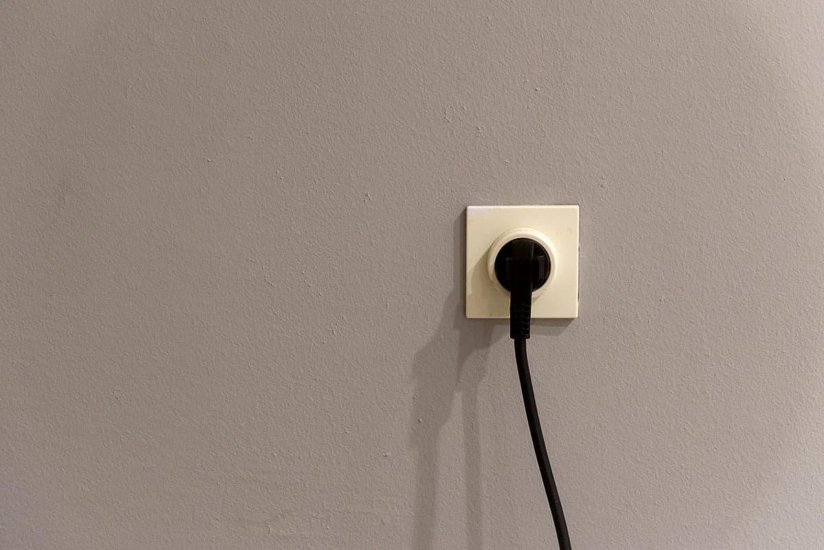 An exterior outlet with a weatherproof cover beside a damp brick wall