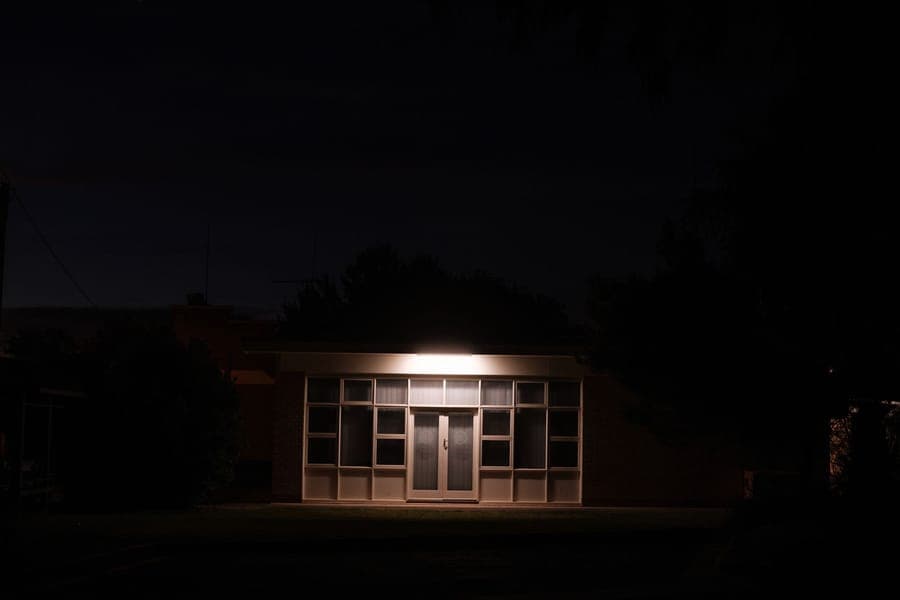 A lit figure standing behind a fogged window in a darkened house